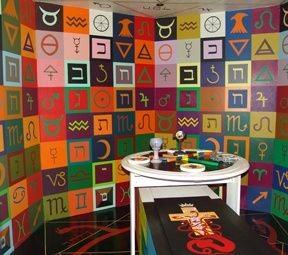 Colourful room painted with zodiac/alchemy glyphs, ritual table